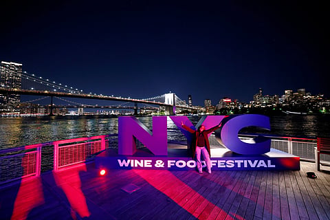 NYC Wine & Food Festival letters on waterfront pier with Brooklyn Bridge & Manhattan skyline behind