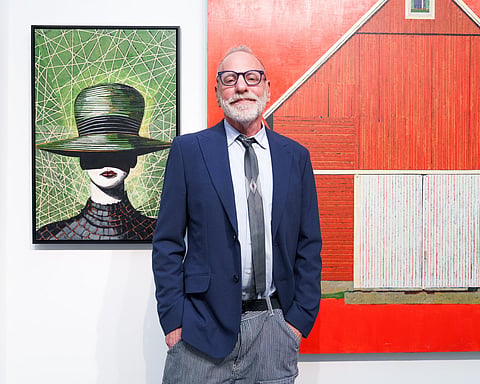 Portrait of artist Don Hershman standing in a gallery with his line-based paintings behind him.