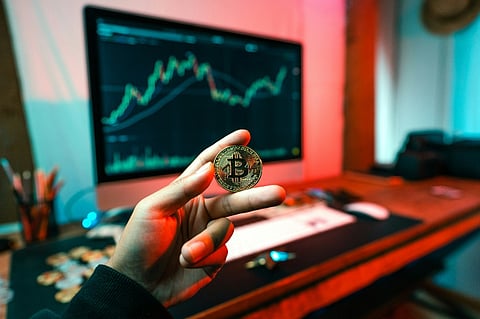 Holding a Bitcoin coin in front of a trading chart.