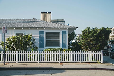 White cottage with blue shutters behind a white picket fence.
