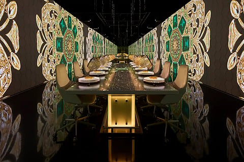 Long dining table in a mirrored room lit with green and gold projected patterns