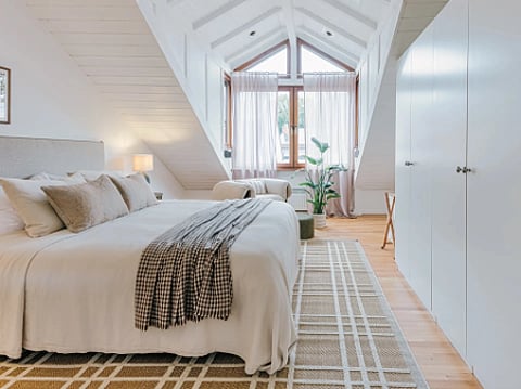 Bright attic bedroom with a bed and white wardrobes.