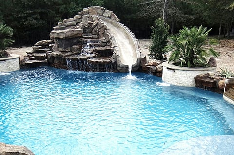 Swimming pool with a stone rock waterfall and water slide.