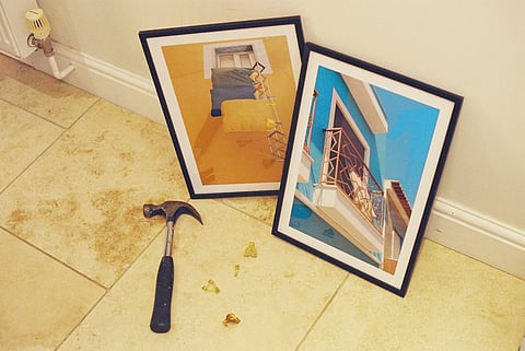 Framed photos with hammer and hanging hardware on a tiled floor.