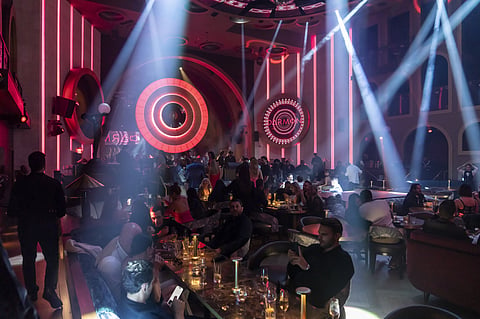 Crowded tables under beams of stage light and glowing red circles in a dark theater room