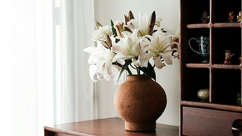 White lilies in a clay vase on a wooden cabinet.