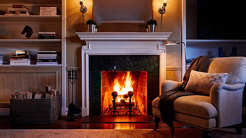 A lit fireplace with candle sconces, bookshelves and an armchair in a hotel suite