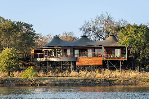 Canvas-roofed lodge on raised platforms on a riverbank lined with trees