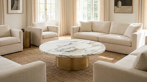 Round marble coffee table surrounded by beige sofas.