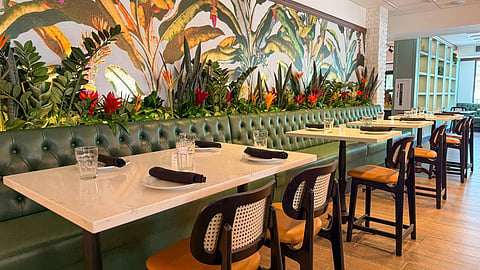 Dining room with green leather banquettes, cane chairs and a tropical botanical mural