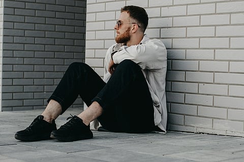 Man sitting on ground against brick wall.
