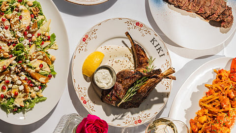 Overhead view of plated lamb chops, salad and fries on a table with a red rose