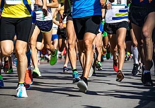 Close-up of runners in colorful athletic clothing and race bibs competing on a sunlit paved road.