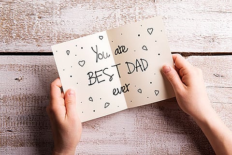 Hands of unrecognizable man holding Fathers Day greeting card. Studio shot on white wooden background.