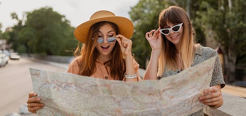 stylish young women traveling together in Europe dressed in spring trendy dresses and accessories smiling happy friends having fun taking photo on camera holding map