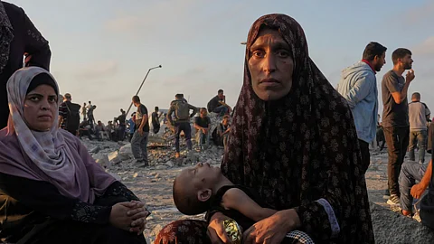 فلسطينية تحتضن طفلها مقتعدة على أحجار وسط تجمع للنازحين في غزة
