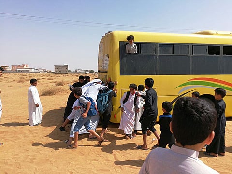 شاهد.. طلاب يدفعون حافلتهم بعدما علقت بمنطقة رملية في جازان