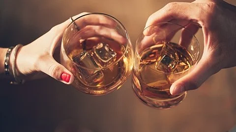 A closeup shot of two people clinking glasses with alcohol at a toast