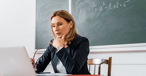 A female teacher sitting at her desk and using a computer during a lesson in the classroom.