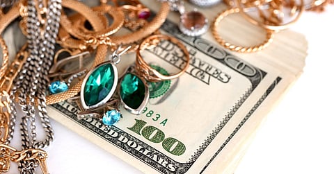 An antique jewelry collection on top of $100 bills. The jewels are a mix of rubies, emeralds, and smoky quartz.