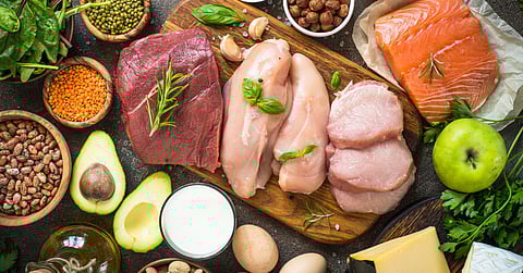 A close up of a table full of various sources of protein. There's avocado, salmon, chicken, eggs, a variety of nuts, and more.