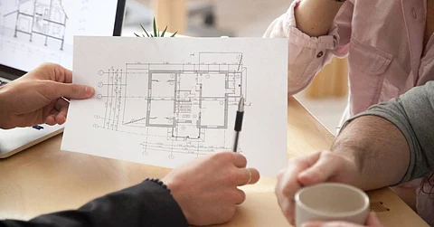 A person in a black blazer shows a couple a piece of paper depicting a floor plan while holding a black pen.