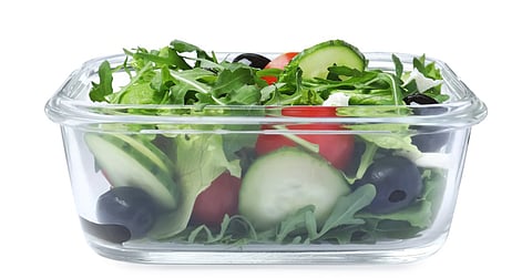 A rectangular glass container contains a salad mixture with cucumbers, black olives, and red cherry tomatoes.