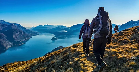 A group of hikers with backpacks and other gear walking in a line on the top of a mountain with a valley in the background.