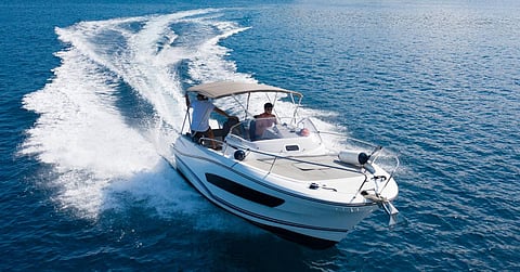 A man driving a high speed motorboat on the open ocean with a sun cover overhead and a large wake behind him.