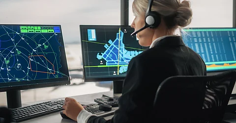 A blonde woman in a white shirt and black blazer speaks into a headset while looking at a flight map.