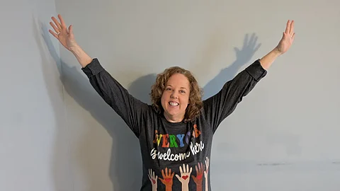 Sheila Applegate with hands in air wearing an Everyone Is Welcome Tshirt