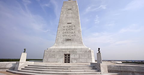 The Wright Brothers Monument standing on a raised stone platform with steps, flanked by busts of the brothers.