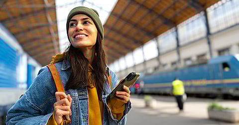 A female traveler holding her phone in her left hand and hanging onto her backpack on her right shoulder. She's smiling.