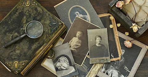 A close-up of a table with family heirlooms, including a book, a box, and photographs of women and babies.