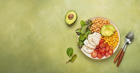 A bowl full of grilled chicken breast, chickpeas, avocado, corn, and tomatoes, accompanied by a fork and spoon.