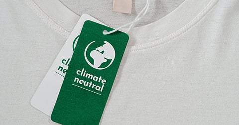 A green tag with white lettering that says “climate neutral” hangs off the tag of a clean, white t-shirt.