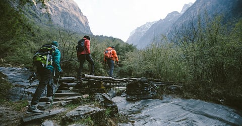 A group of three people wearing coats and backpacks while hiking through the wilderness on a foggy day.