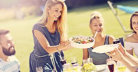 A woman serves a salad to her guests at an outdoor backyard party. A string of lights hangs in the background.