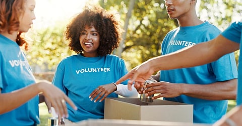 A group of people wearing blue shirts with the word “Volunteer” on them pack up boxes with canned goods.