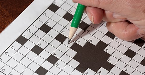 Close-up of a woman's hand holding a pencil as she does a crossword puzzle. The pencil in her hand is green.