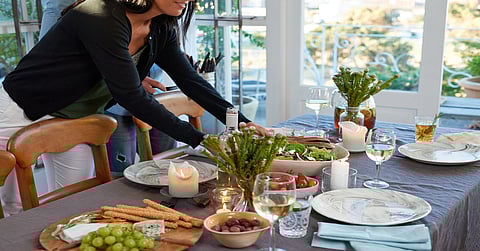 A woman sets a table with various food items for a dinner party. She has the plates and glasses on the table.
