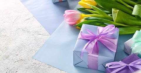A close-up of a group of boxes wrapped in pastel wrapping paper and bows next to a pile of spring tulips.