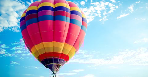 A large hot air balloon with red, blue, and yellow stripes floats in the sky. A few clouds drift off in the distance.