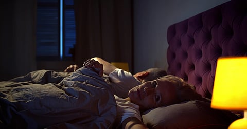 A man and woman laying next to each other in bed. The man has rolled over while the woman has her eyes open.