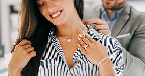 A close-up of a young woman receiving a necklace as a gift from her partner. He places it around her neck.