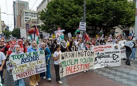 A large crowd of protesters marches through a city street in support of Palestine, holding banners and signs. The front banners read "Washington Muslim Youth 4 Palestine" and "Today We Are All Aysenur," referencing Aysenur Ezgi Evgi, with "Murdered" written underneath. Participants hold Palestinian flags and signs denouncing Israeli actions, including messages like "Israel bombs, U.S.A. pays!"