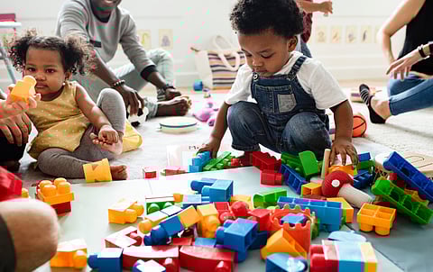 Children playing with toys, particularly large, colorful building blocks that are on the floor around them.