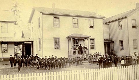 A historical photo of the Puyallup Indian School, with students standing outside in rows to pose for the photo.