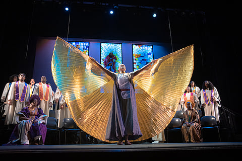 Dancer Kearia Keke Duncan performs in last year’s production, raising her garment with outstretched arms to create the shape of wings; other performers and stained-glass windows are visible behind her.