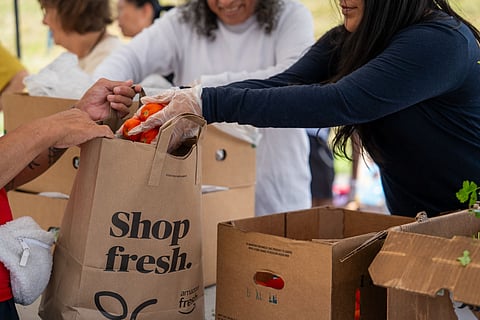 Image of a person handing a bag of food and groceries to another person.  Others are in the background.